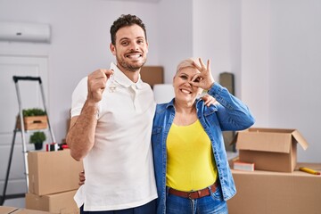 Wall Mural - Hispanic mother and son holding keys of new home smiling happy doing ok sign with hand on eye looking through fingers