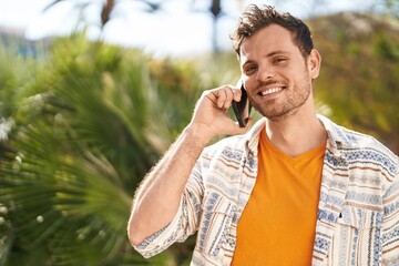 Wall Mural - Young hispanic man smiling confident talking on the smartphone at park