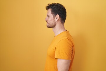 Sticker - Young hispanic man standing over yellow background looking to side, relax profile pose with natural face and confident smile.