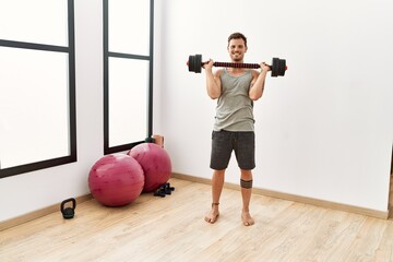 Wall Mural - Young hispanic man smiling confident training using dumbbells at sport center