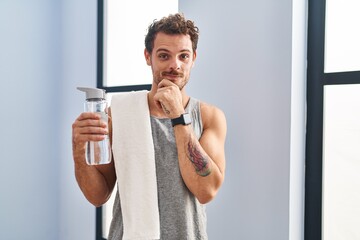 Poster - Young hispanic man wearing sportswear drinking water looking confident at the camera smiling with crossed arms and hand raised on chin. thinking positive.