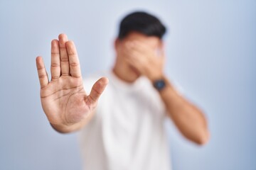 Canvas Print - Hispanic man standing over blue background covering eyes with hands and doing stop gesture with sad and fear expression. embarrassed and negative concept.