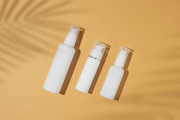 Wall Mural - Skincare beauty concept. Flat lay photo of pump cosmetics bottles without label and tropical leaves shadow on sandy background. Beauty cosmetics mockup idea.