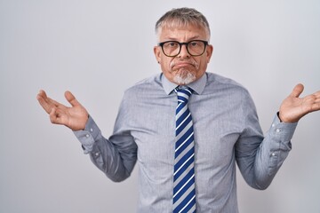 Poster - Hispanic business man with grey hair wearing glasses clueless and confused expression with arms and hands raised. doubt concept.