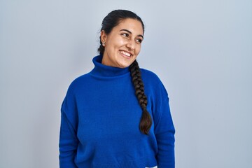 Sticker - Young hispanic woman standing over isolated background looking away to side with smile on face, natural expression. laughing confident.