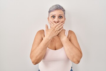 Poster - Middle age caucasian woman standing over white background shocked covering mouth with hands for mistake. secret concept.