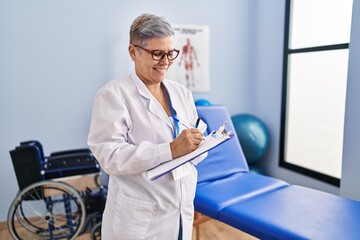 Wall Mural - Middle age woman physiotherapist writing on clipboard at rehab clinic