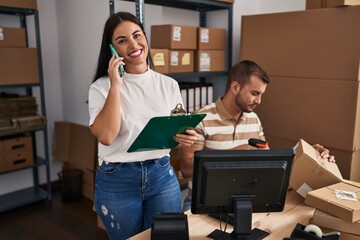 Canvas Print - Man and woman business workers talking on the smartphone and scanning label using barcode reader at storehouse