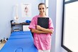 © Krakenimages.com - Young hispanic woman wearing physiotherapist uniform holding clipboard at physiotherpy clinic