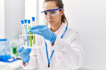 Poster - Young hispanic woman wearing scientist uniform holding test tube at laboratory