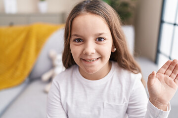 Poster - Adorable hispanic girl sitting on sofa saying hello with hand at home