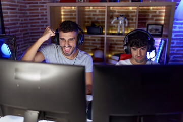 Canvas Print - Two hispanic men streamers playing video game with winner expression at gaming room