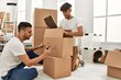 © Krakenimages.com - Two hispanic men couple smiling confident packing book cardboard box at new home