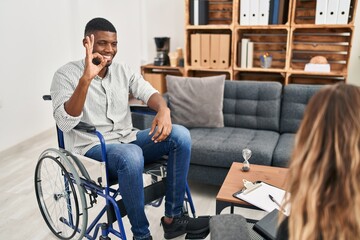 Canvas Print - African american man doing therapy sitting on wheelchair smiling positive doing ok sign with hand and fingers. successful expression.