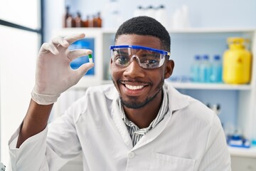 Wall Mural - Young african american man wearing scientist uniform holding pill at laboratory