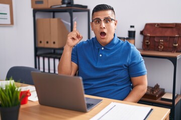 Canvas Print - Young hispanic man working at the office with laptop pointing finger up with successful idea. exited and happy. number one.