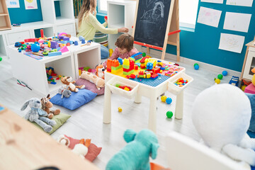 Poster - Teacher and toddler playing with construction blocks sitting on table at kindergarten