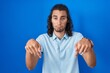 © Krakenimages.com - Young hispanic man standing over blue background pointing down looking sad and upset, indicating direction with fingers, unhappy and depressed.