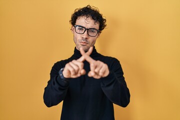 Poster - Hispanic man standing over yellow background rejection expression crossing fingers doing negative sign