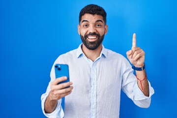 Poster - Hispanic man with beard using smartphone typing message smiling amazed and surprised and pointing up with fingers and raised arms.