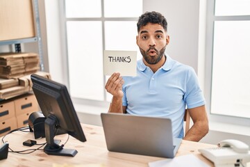Wall Mural - Hispanic man with beard working at the office with laptop holding thanks banner scared and amazed with open mouth for surprise, disbelief face