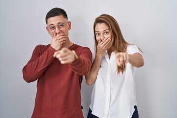 Canvas Print - Mother and son standing together over isolated background laughing at you, pointing finger to the camera with hand over mouth, shame expression