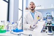 © Krakenimages.com - Hispanic man working at scientist laboratory holding blank clipboard angry and mad screaming frustrated and furious, shouting with anger looking up.