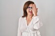 © Krakenimages.com - Middle age hispanic woman standing over isolated background covering one eye with hand, confident smile on face and surprise emotion.