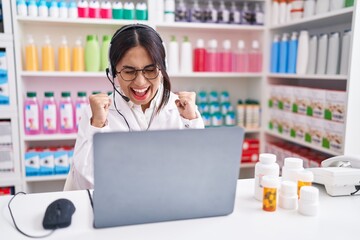 Wall Mural - Young arab woman working at pharmacy drugstore using laptop excited for success with arms raised and eyes closed celebrating victory smiling. winner concept.