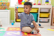 © Krakenimages.com - African american boy holding wooden piece sitting on floor at kindergarten