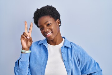 Sticker - African american woman standing over blue background smiling looking to the camera showing fingers doing victory sign. number two.