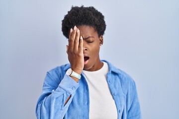 Wall Mural - African american woman standing over blue background yawning tired covering half face, eye and mouth with hand. face hurts in pain.