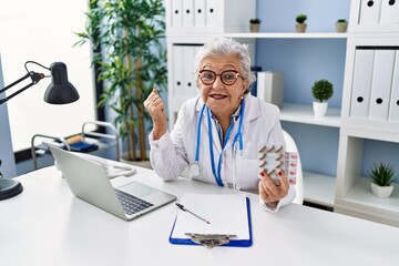 Wall Mural - Senior woman with grey hair wearing doctor uniform holding prescription pills screaming proud, celebrating victory and success very excited with raised arm