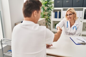 Middle age man and woman doctor and patient shake hands having medical consultation at clinic