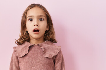 Little hispanic girl standing over pink background scared and amazed with open mouth for surprise, disbelief face