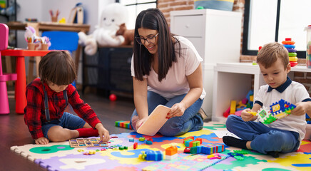 Poster - Teacher with boys playing with maths puzzle game sitting on floor at kindergarten