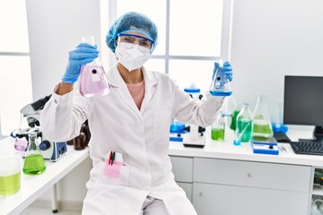 Wall Mural - Young latin woman wearing scientist uniform holding test tubes at laboratory