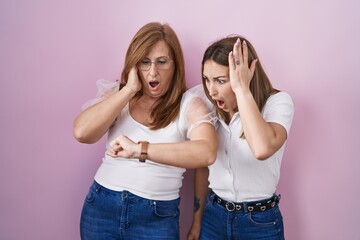 Wall Mural - Hispanic mother and daughter wearing casual white t shirt over pink background looking at the watch time worried, afraid of getting late