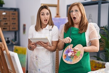 Wall Mural - Hispanic mother and daughter painting at paint studio in shock face, looking skeptical and sarcastic, surprised with open mouth