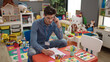 © Krakenimages.com - Young hispanic man preschool teacher talking on smartphone writing on document at kindergarten