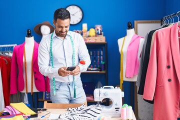 Sticker - Young hispanic man tailor smiling confident using smartphone at sewing studio