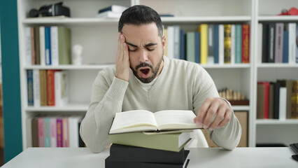 Sticker - Young hispanic man student reading book yawning at library university