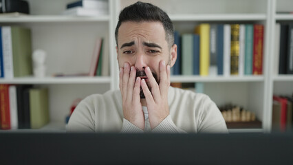 Sticker - Young hispanic man student using computer stressed at library university