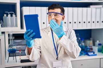 Wall Mural - Non binary person working at scientist laboratory using tablet covering mouth with hand, shocked and afraid for mistake. surprised expression