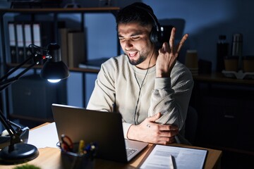 Canvas Print - Young handsome man working using computer laptop at night smiling with happy face winking at the camera doing victory sign. number two.