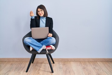 Young hispanic woman sitting on chair using computer laptop doing italian gesture with hand and fingers confident expression