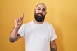 © Krakenimages.com - Young hispanic man with beard and tattoos standing over yellow background showing and pointing up with finger number one while smiling confident and happy.