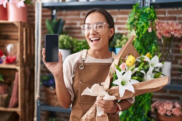 Sticker - Young hispanic woman working at florist shop showing smartphone screen winking looking at the camera with sexy expression, cheerful and happy face.