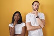 © Krakenimages.com - Interracial couple standing over yellow background with hand on chin thinking about question, pensive expression. smiling and thoughtful face. doubt concept.