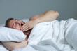 © Евгений Шемякин - Young happy handsome sleepy man in the bed in bedroom at home in the morning lying under white blanket, enjoy resting, sleep well and yawn with opened mouth